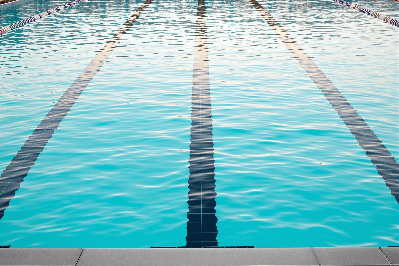 An empty outdoor swimming pool lane with calm turquoise water in morning light